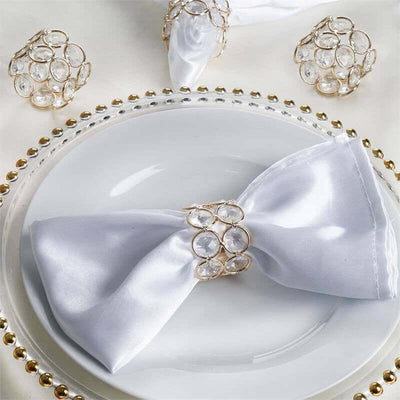 Elegant white satin napkin with crystal ring on a decorative plate.