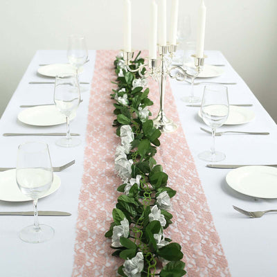Table setting with a pink lace runner and green floral accents.