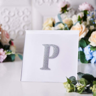 Silver glitter letter "P" on a clear acrylic display with floral background.