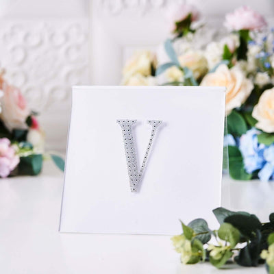 Silver rhinestone letter "V" on a white card with floral background.