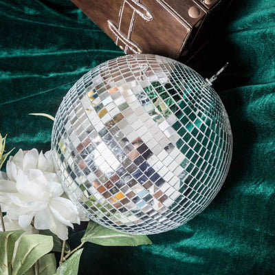 Mirrored disco ball surrounded by flowers and greenery on green velvet fabric.