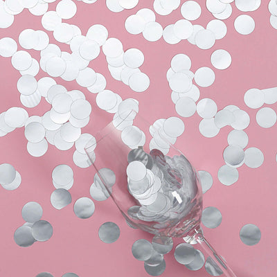 Silver confetti scattered around a clear glass on a pink background.