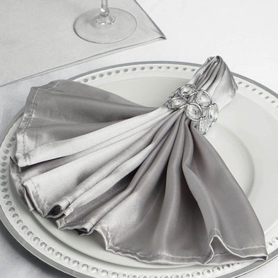 Elegant gray satin napkin with jeweled ring on a decorative plate.