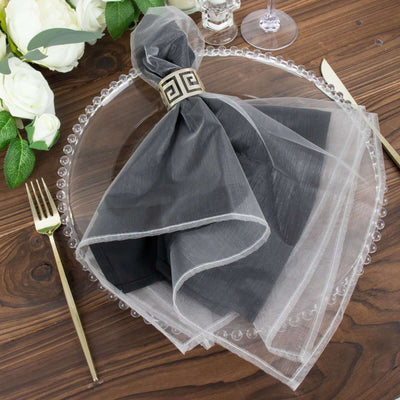 Elegant black napkin with sheer overlay and decorative ring on a wooden table setting.