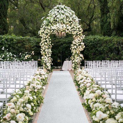 Elegant wedding arch adorned with white flowers and greenery, set in a garden venue.