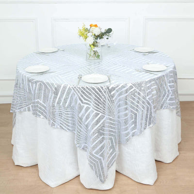 Round table set with a silver patterned tablecloth and white plates.