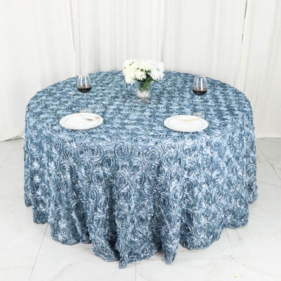 Round blue rose-patterned tablecloth on a dining table with plates and glasses.
