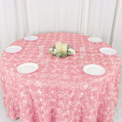 Pink rose-patterned tablecloth on a round table with plates and candles.