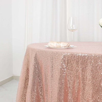 Rose gold sequin tablecloth draping over a table with a glass and napkin.