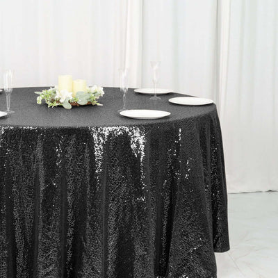 Black sequin tablecloth draped over a round table with plates and candles.