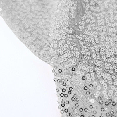 Silver sequin fabric draping elegantly on a white background.