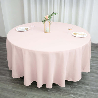 Round pink tablecloth draped over a round table set for dining.