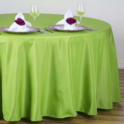 Green tablecloth draping over a round table set with elegant dinnerware and napkins.
