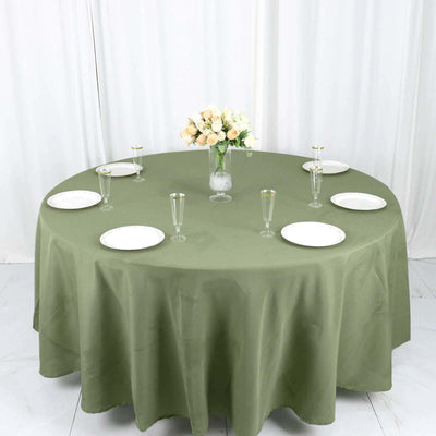 Round olive green tablecloth set for dining with plates and glasses.