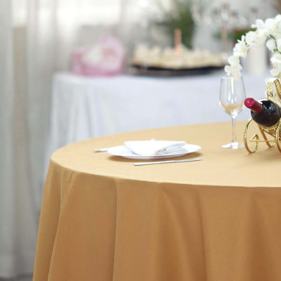 Elegant gold tablecloth draped over a round table with wine and dinnerware.