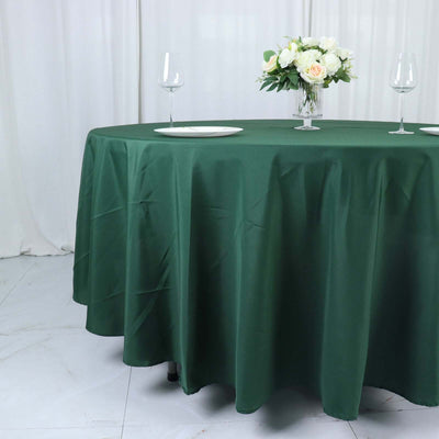 Green tablecloth draped elegantly on a round table with floral centerpiece and glasses.