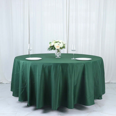 Green round tablecloth draping over a table set for dining with floral centerpiece.
