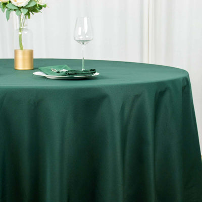 Green round tablecloth on a dining table with a vase and glass.