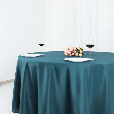 Teal tablecloth draped over a round table with wine glasses and flowers.