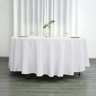 Round white tablecloth on a table with a vase and flowers.