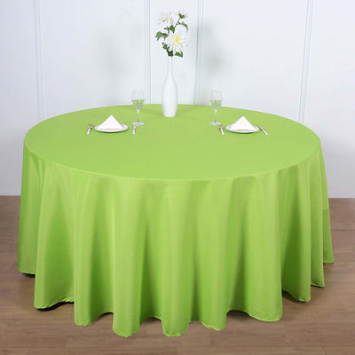 Round green tablecloth draped over a table with decor and tableware.