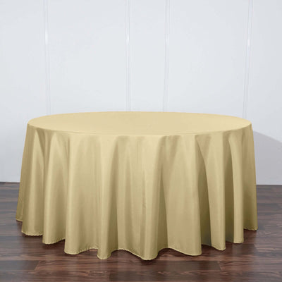Round gold tablecloth draping over a circular table on a wooden floor.