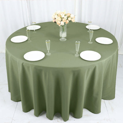 Round olive green tablecloth with plates and glasses set for dining.