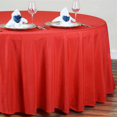 Red round tablecloth draping over a table set for dining.