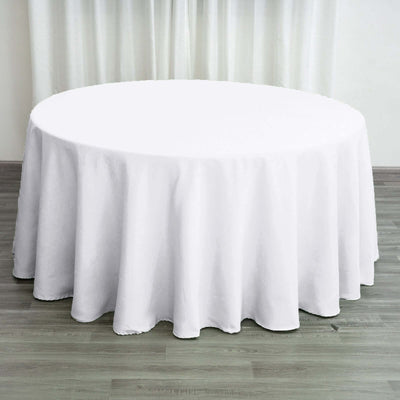 Round white tablecloth on a wooden floor with curtains in the background.