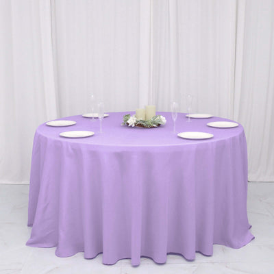 Round lavender tablecloth draped over a table with plates and candles.