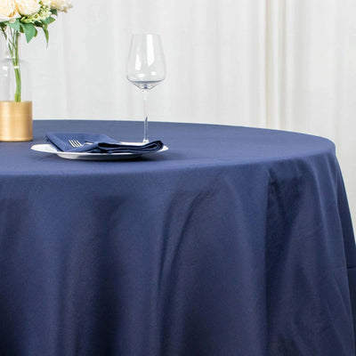 Navy blue tablecloth on a round table with a glass and napkin set.