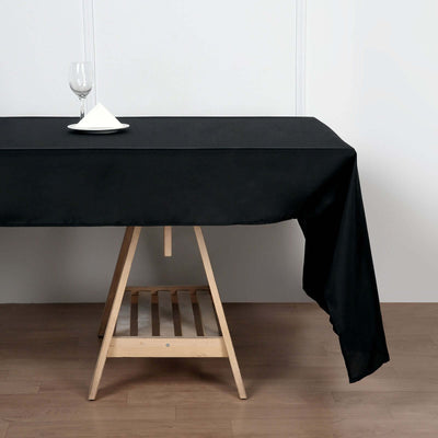 Black tablecloth draped over a wooden table with a glass and plate on top.