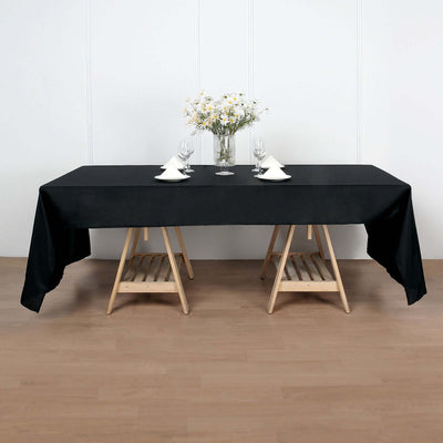 Black tablecloth draped over a wooden table set for dining with flowers.