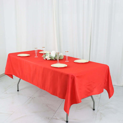 Red tablecloth draped over a table set with plates and candles.