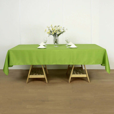 Green tablecloth draped over a wooden table with floral centerpiece and glassware.