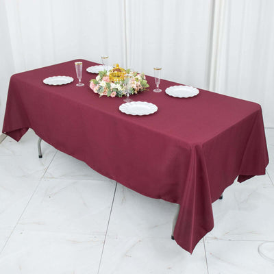 Burgundy tablecloth draped over a table set with plates and floral centerpiece.