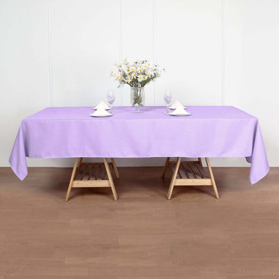 Purple tablecloth on a wooden table set for dining with flowers and glassware.