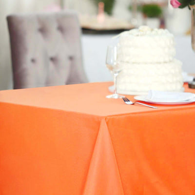 Orange tablecloth draped over a table with a wedding cake and glassware.