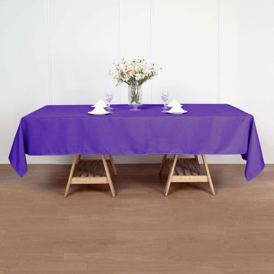 Purple tablecloth on a wooden table with white decor elements and flowers.
