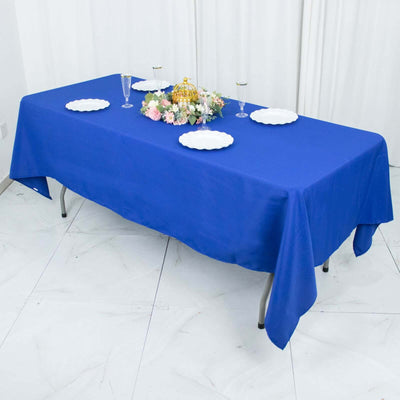 Blue tablecloth set for a dining table with plates and floral centerpiece.