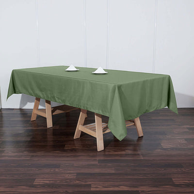 Green tablecloth on a wooden table with two napkin folds.
