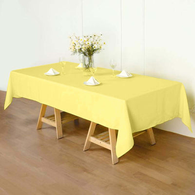 Yellow tablecloth on a wooden table set for dining with glasses and napkins.