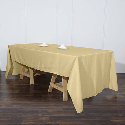 Beige tablecloth draped over a wooden table with napkin folds.
