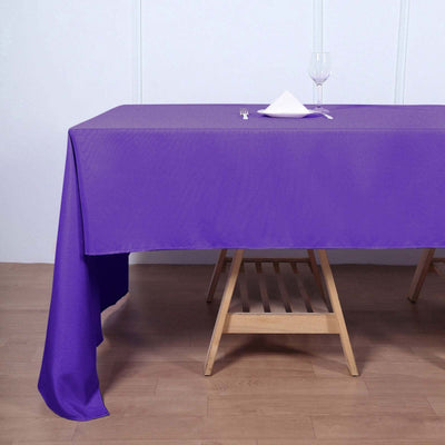 Purple tablecloth draped over a wooden table with a glass and napkin.