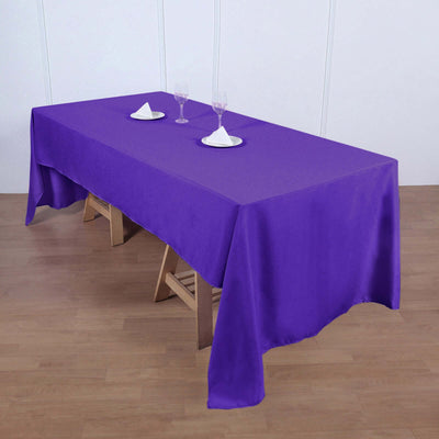 Purple tablecloth draped over a wooden table with white plates and glasses.