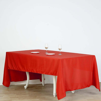 Red tablecloth draping over a white table with plates and glasses on top.