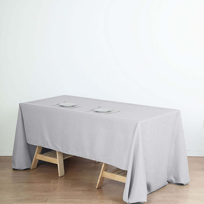 Gray tablecloth on a wooden table with plates, set against a plain backdrop.
