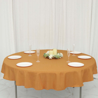 Round table set with plates and candles on a brown tablecloth in a staged setting.