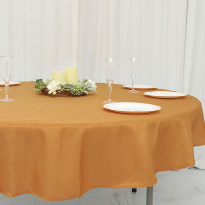Round orange tablecloth on a dining table set with plates and glasses.