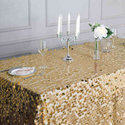 Gold sequin tablecloth on a decorated dining table with candles and flowers.